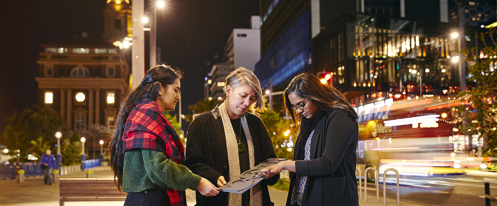 Three landscape architecture students stand on Auckland's Quay street examing the panel design artwork.