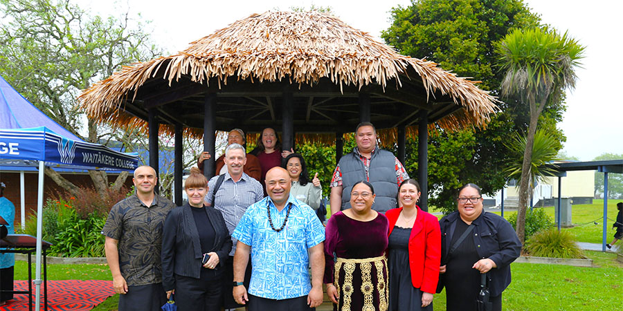 Group of staff and Unitec visitors smile warmly while posing in front of the Waitākere college fale