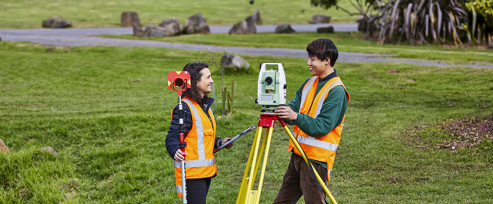 Two students operating a total station machine in the outdoor environment next to a stream
