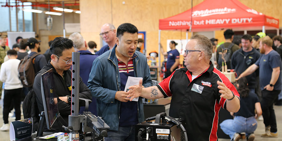 Exhibitor explains enthusiastically about a welding machine to attendees at career expo