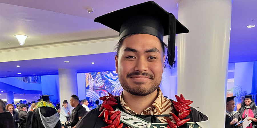 Ethan Hansell-Hunt stands in graduation regalia proudly holding his qualification certificate at at his Unitec graduation ceremony