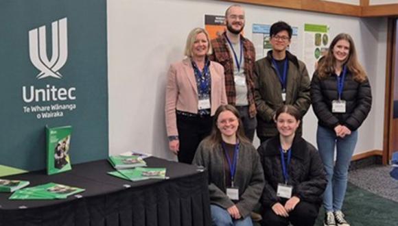 Five of Unitec's biosecurity ākonga along with one of their tutors in front of a Unitec banner