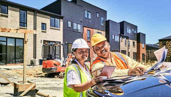 two construction workers reviews plans on the bonnet of a ute while looking out at a cosntruction site