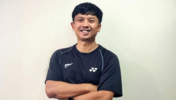 Dhanny Oud stands in front of plain background smiling at the camera with his arms crossed