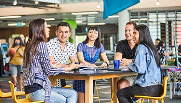 Group of five students talking around a standing table