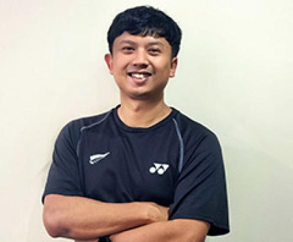 Dhanny Oud stands in front of plain background smiling at the camera with his arms crossed