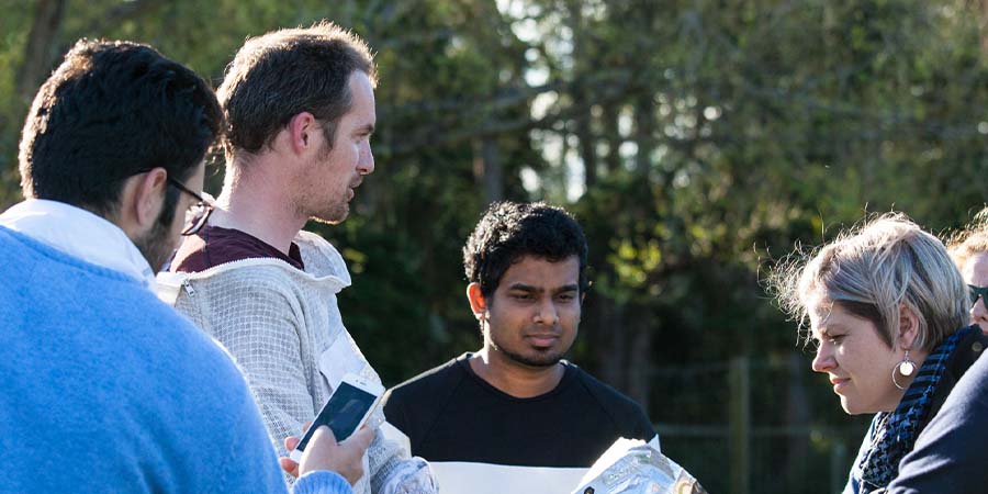 Business students standing outside with a beekeeper.