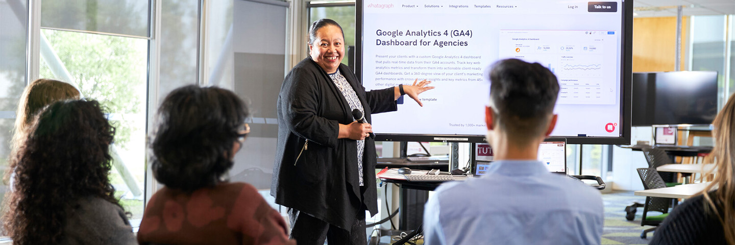 A woman gives a presentation on a digital screen to a group of colleagues.