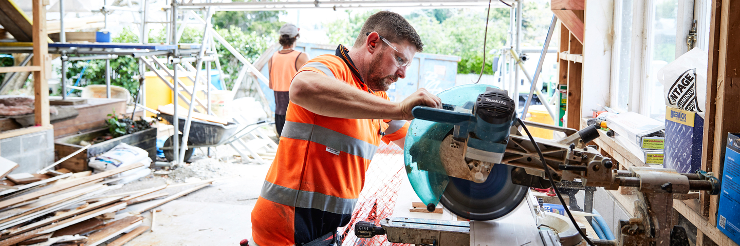 A man in a high-vis vest and safety goggles works with a large circular saw.