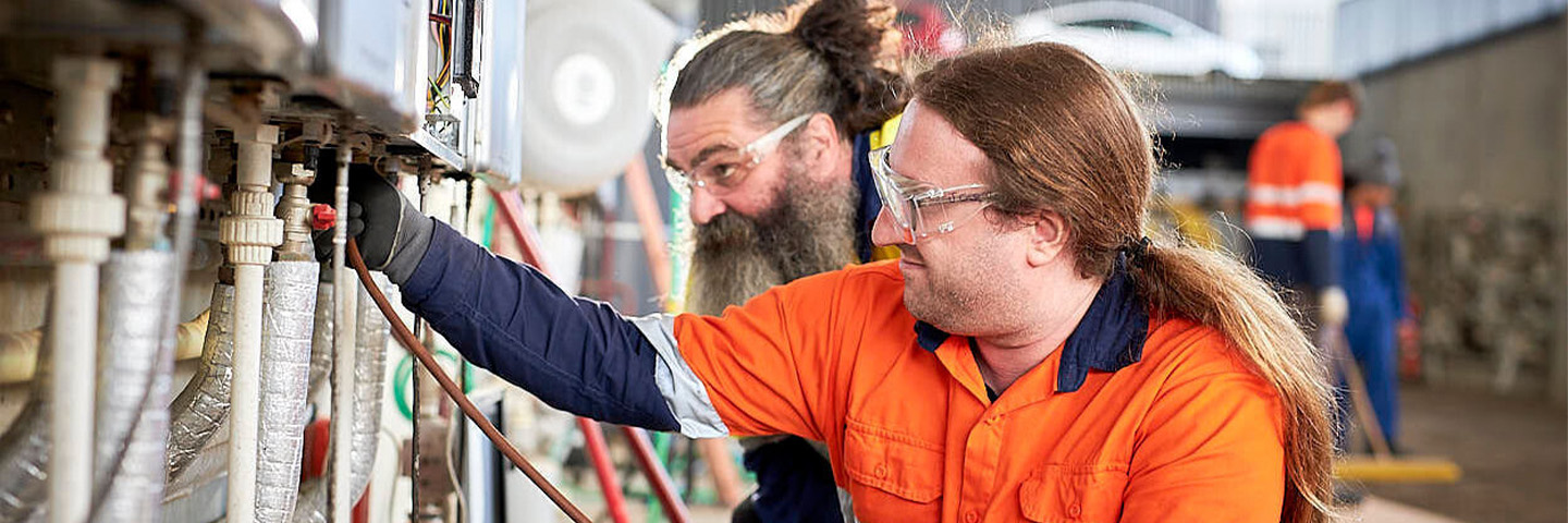 A student works on some pipes while their tutor supervises.