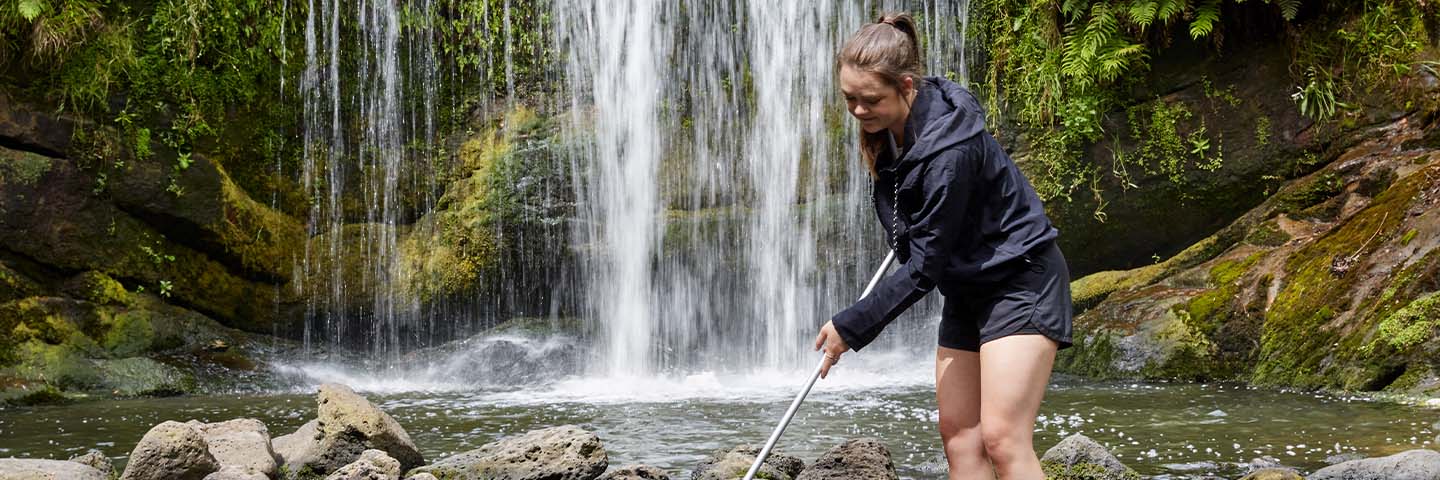 A young woman uses a net in water in front of a waterfall.