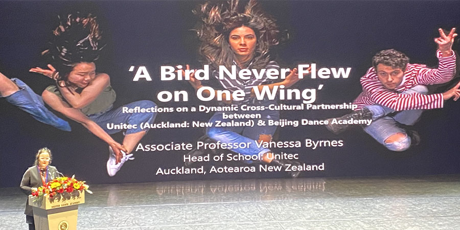 Prof. Vanessa Byrnes stands behind a lectern giving a presentation entitled 'A bird never flew on one wing'.
