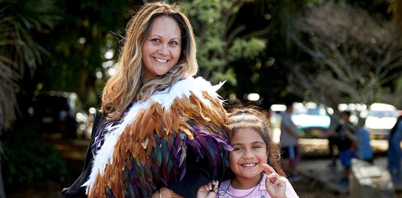 Krystle Miller wears a korowai and smiles for the camera alongside her daughter.