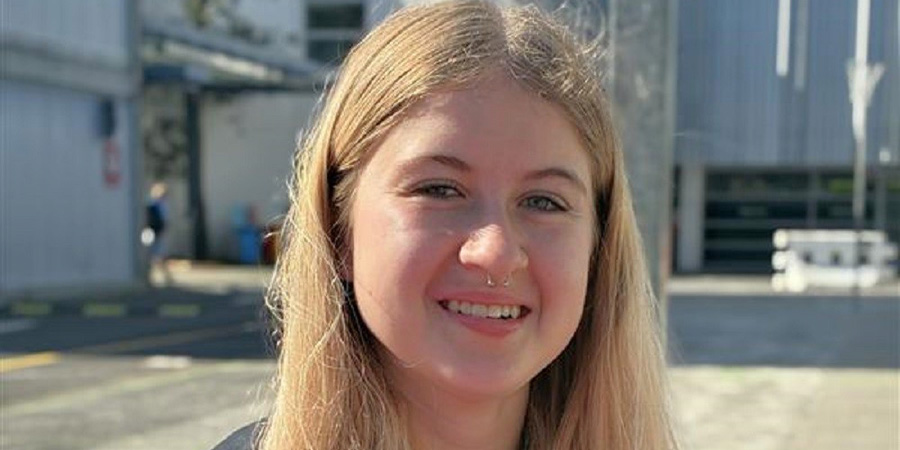 Brooke Wilson, a blonde woman with long hair, smiles in front of university buildings.