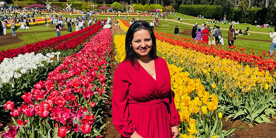 Parul stands in a park with with rows of colourful tulips and miniature windmills in the background