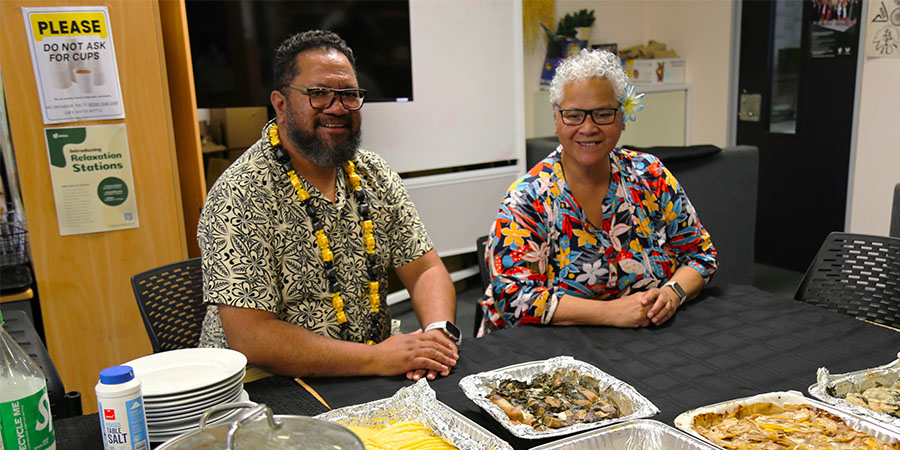 Niuean kaimahi smile behind a table of Niuean food.