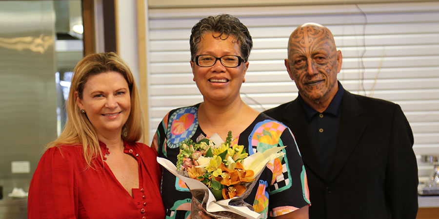 Dr Roseanne Ellis and Kaihaūtu Harawira Pearless stand on either side of winner Maureen Fepuleai, who is holding a bouquet of flowers.