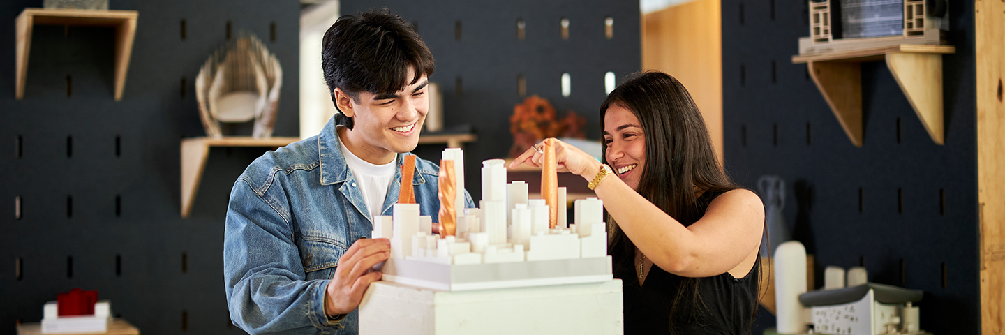 Two architecture students explore a physical scale model of a group of buildings