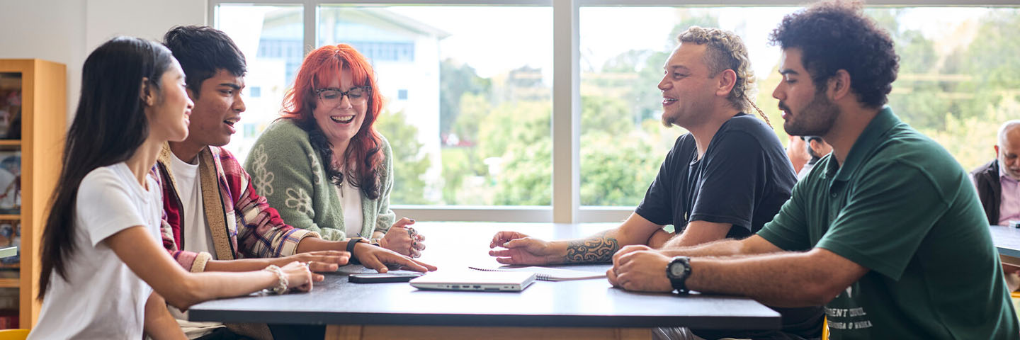 A group of students talk and laugh around a table.