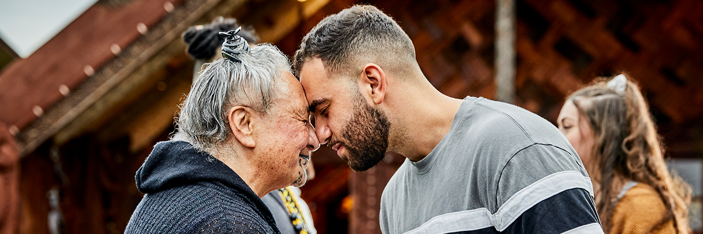 Two people share a hongi in front of the wharenui at Unitec Te Noho Kotahitanga marae