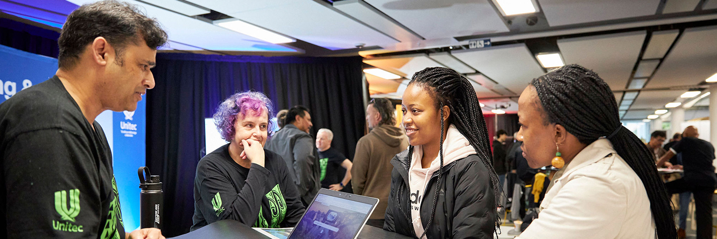 Unitec staff member talks to students while using a laptop