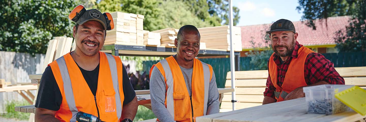 Three diverse workers in high-visibility vests relax in the sunshine.