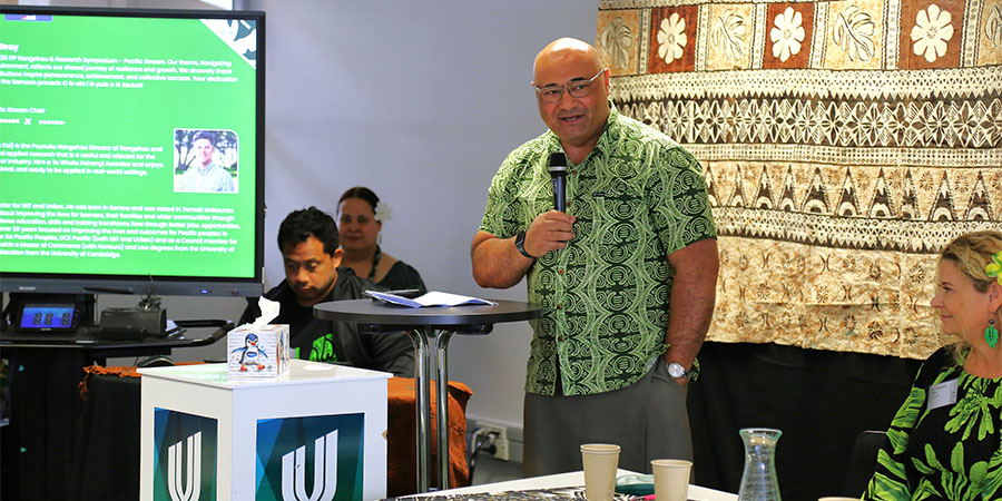 Unitec Executive Director Peseta Sam Lotu-Iiga stands holding a mircophone to address the ITP research symposium.