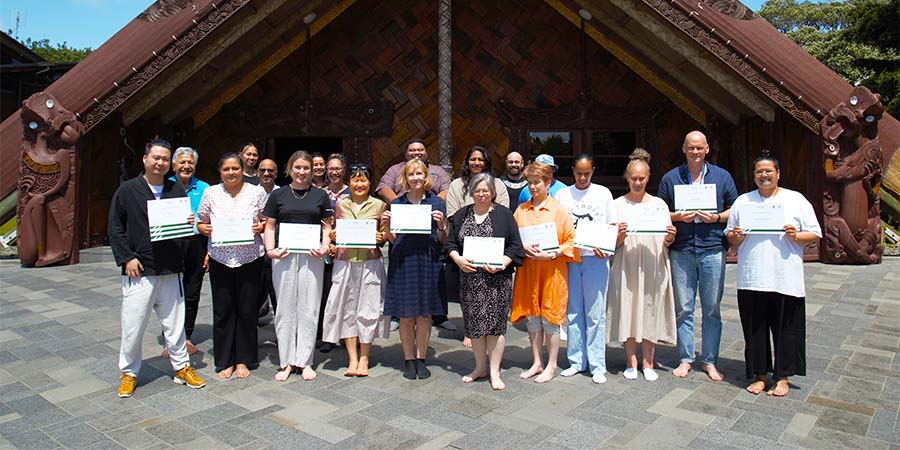 Kaimahi who have completed micro-credentials pose with their certificates outside Unitec's Marae meeting house.