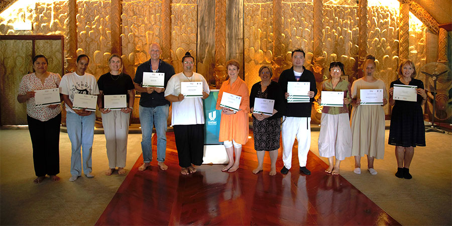 Kaimahi pose with their micro-credential certificates inside Unitec's Marae meeting house.