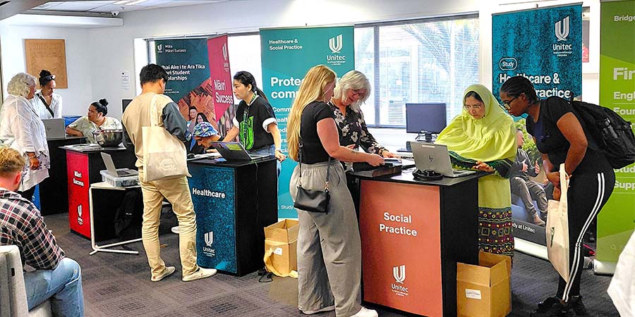 People stand chatting at booths during Info and Enrolment Day at Waitākere campus. 