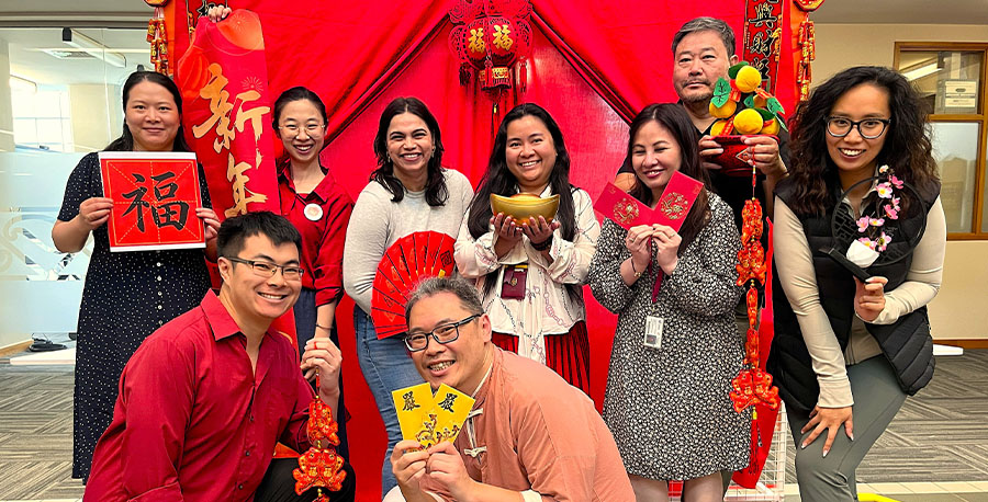 A group of Unitec staff pose in front of a bright backdrop with lanterns.