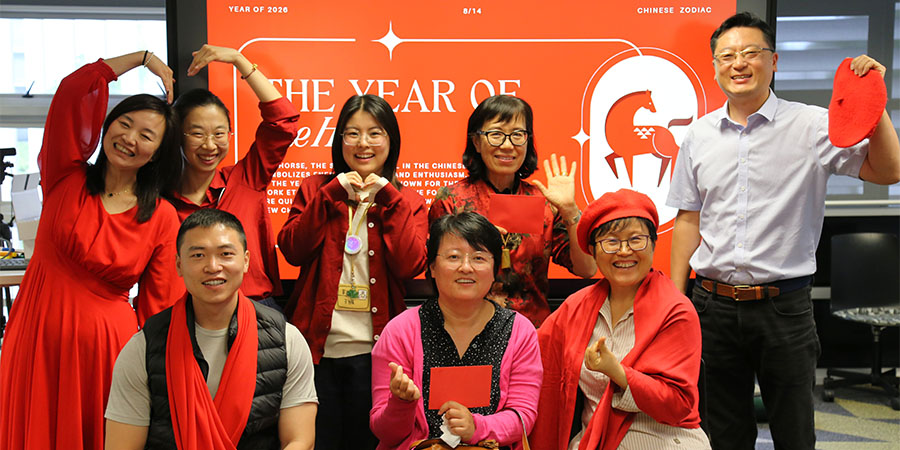 A group of staff pose in front of a digital screen with information about the Year of the Fire Horse.