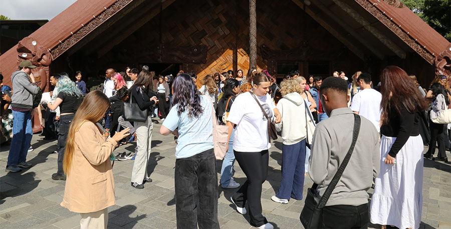 Students and whānau mingle outside te wharenui o Te Noho Kotahitanga Marae.