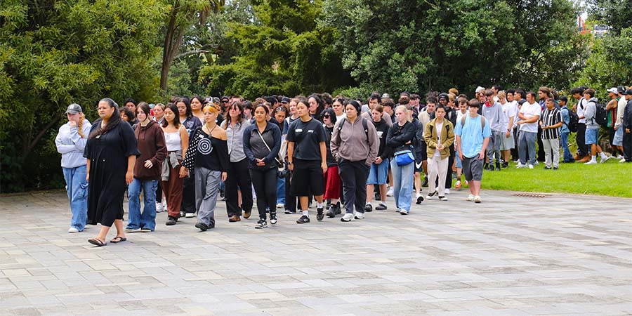 A large crowd of students and whānau walk towards the wharenui during the welcome pōwhiri.