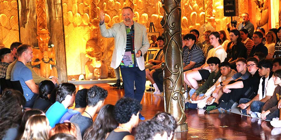 A lecturer gives a speech to students seated on the floor in te wharenui o Te Noho Kotahitanga Marae.