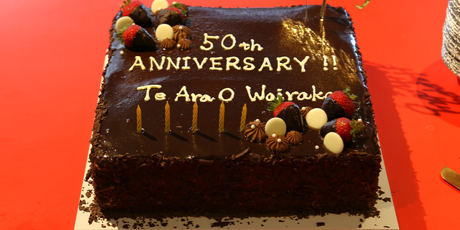 A large chocolate cake iced with '50th anniversary Te ara o Wairaka'.