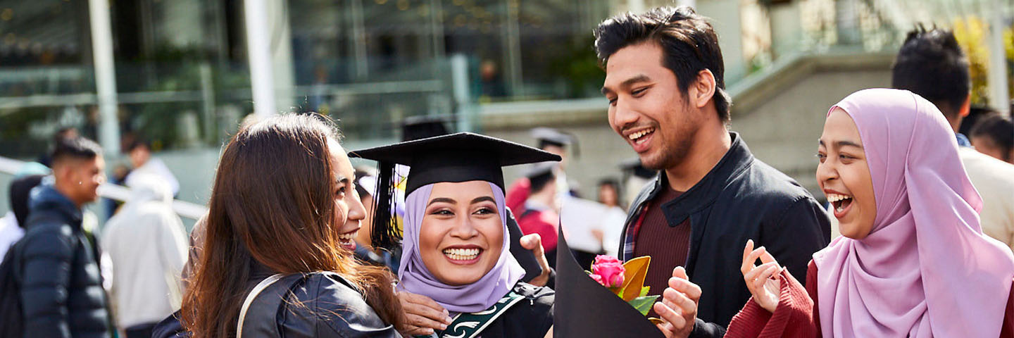 A woman in graduation attire celebrates with friends.