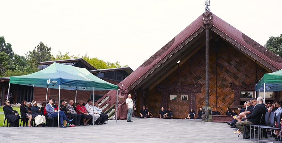 Graduates, staff and guests seated under gazebos outside te wharenui.