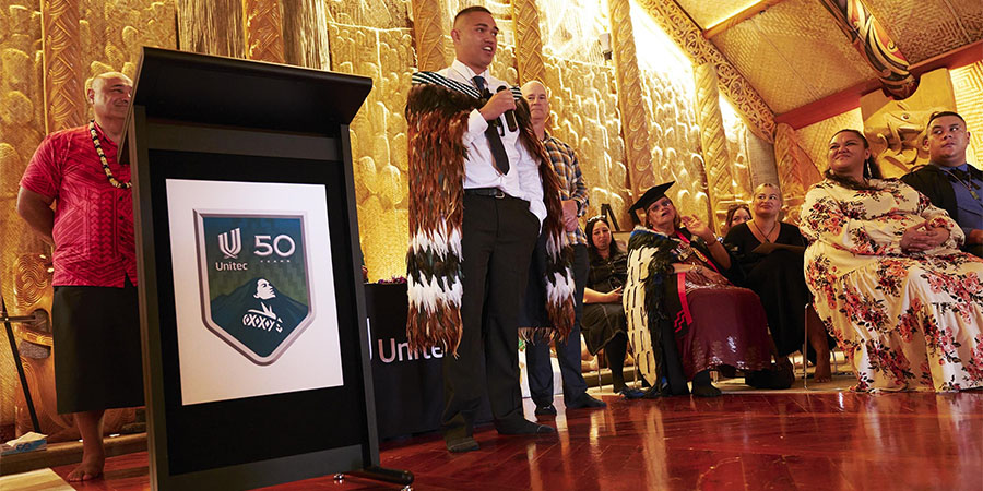 A man in a korowai gives a speech inside te wharenui o te Noho Kotahitanga Marae.