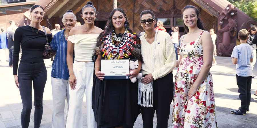A Māori graduate in traditional attire poses for a photo with her family.