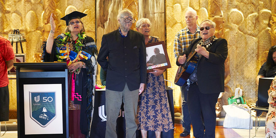 A group sing accompanied by guitar inside te wharenui.