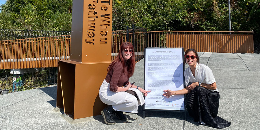 Two people crouch down next to a display of some text, in front of the sculptural marker.