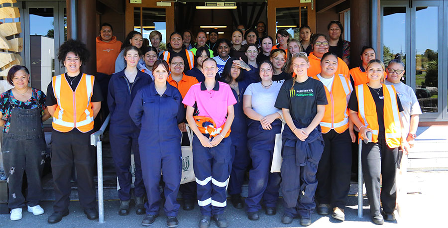 Attendees at a Wahine in trades event pose for a photo outside the wharekai at Te Noho Kotahitanga Marae.