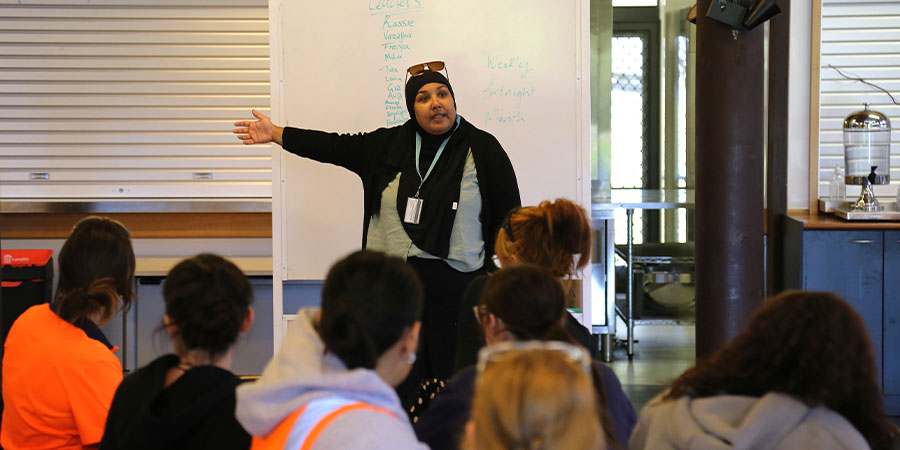 A group of women listen to a lecturer in a hijab.