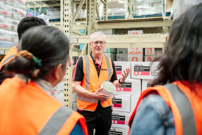 A Gilmour's staff member in a high-vis vest talks to a group of students.