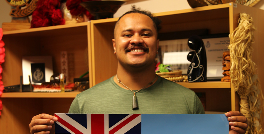 Ian Ratusau holds up a flag while smiling for the camera.