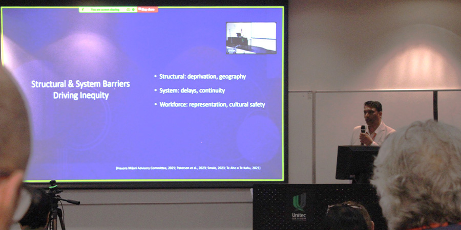 A presenter gives a talk in front of a large digital screen.