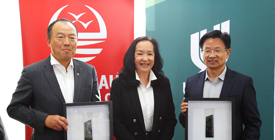 Professor Christina Hong stands between two of the Chinese delegates, each holding a framed taonga.