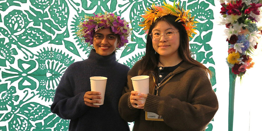 Two students in traditional Cook Islands floral headwear hold cups and smile for the camera.