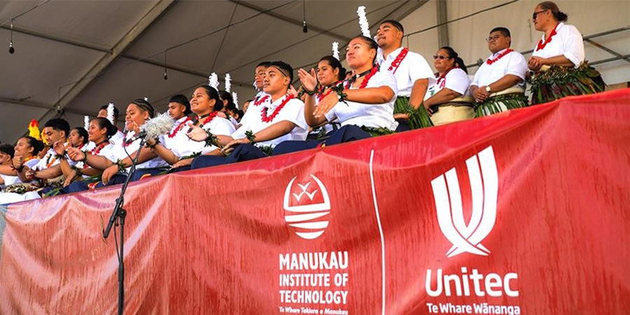 Students in traditional Tongan garb perform at Polyfest behind an MIT and Unitec banner.